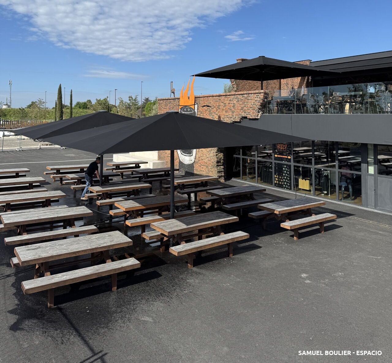 Terrasse basse du Hellcity, bancs en bois brut et parasols noirs.